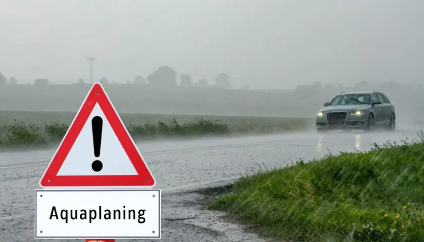 Señal de advertencia de aquaplaning en un día lluvioso. Un coche circula por la carretera mojada. ¿Qué puede hacer para evitar el aquaplaning?