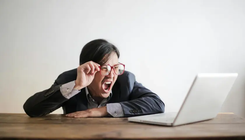 Mann mit Brille schreit frustriert vor Laptop. Vielleicht lernt er gerade, wie funktioniert ein Fernstudium, und ist überfordert.