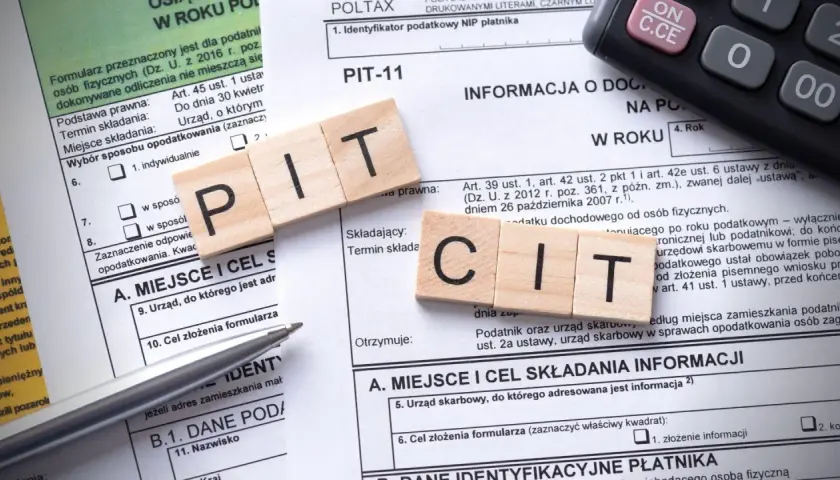 Drewniane klocki z literami PIT i CIT leżą na formularzach podatkowych. Temat: podatek od sprzedaży nieruchomości po upływie 5 lat.