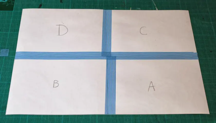 Papier divisé en quatre sections (A, B, C, D) par du ruban adhésif bleu rayé, prêt à créer un motif.