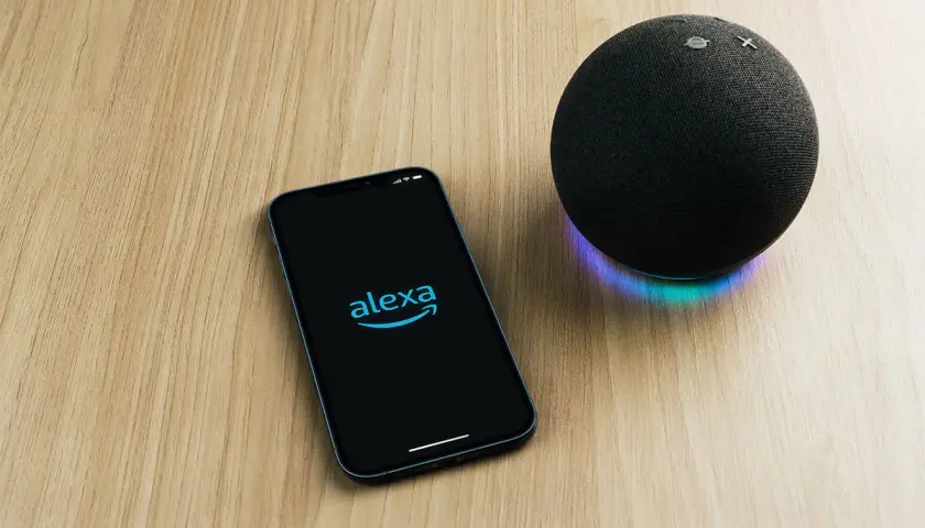 Telefon z logo Alexa i głośnik Echo na drewnianym blacie. Chcesz wiedzieć, alexa co to?