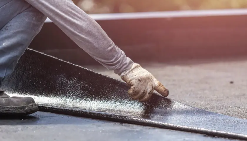 Hand mit Handschuh legt neue Dachpappe an. Alte Dachpappe entsorgen ist wichtig für die Langlebigkeit.