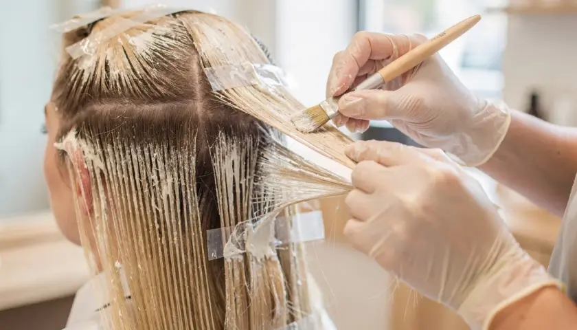 Manos enguantadas aplican tinte para crear mechas blancas en cabello rubio.