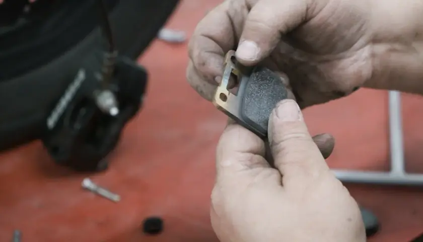 Manos sucias sostienen una pastilla de freno de moto lista para el cambio.