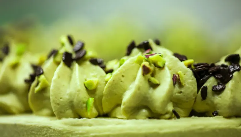 Puszysty krem pistacjowy do tortu, ozdobiony kawałkami pistacji i czekolady.