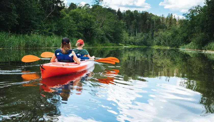 Dwie osoby płyną kajakiem po spokojnej rzece, otoczonej zielenią. Idealne miejsce na spływ kajakowy Mazury, gdzie najlepiej poczuć bliskość natury.