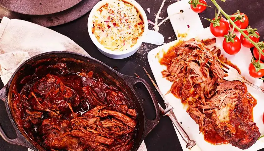Saftigt pulled beef i en gjutjärnsgryta, serverat med krämig coleslaw och färska tomater. Perfekt för en mysig middag.