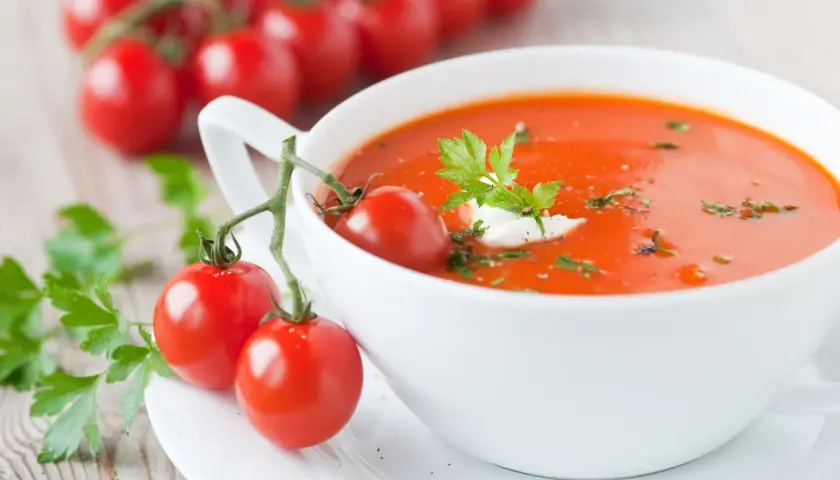 Zupa pomidorowa, ozdobiona gałązką pomidorków i natką pietruszki, wygląda apetycznie. Ile waży zupa pomidorowa? To zależy od porcji!