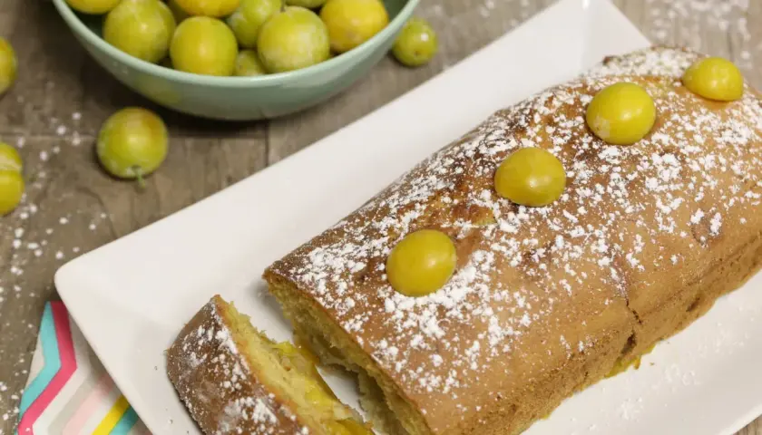 Gâteau lorrain aux mirabelles, saupoudré de sucre glace, avec des mirabelles fraîches sur le dessus et dans une coupelle à côté.