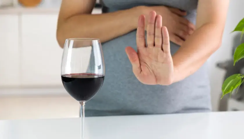 Kobieta w ciąży odrzuca kieliszek czerwonego wina, mówiąc "nie" alkoholowi.