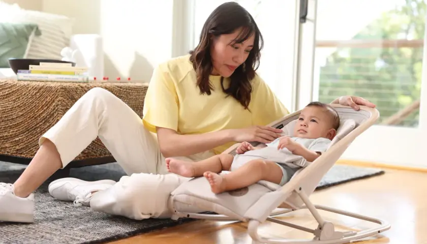En kvinna sitter på golvet bredvid en bebis i en babysitter från Maxi-Cosi.
