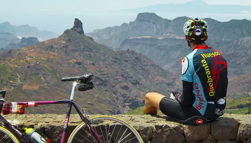 Ciclista descansa tras explorar rutas en bici Gran Canaria. Paisaje montañoso y su bicicleta morada.