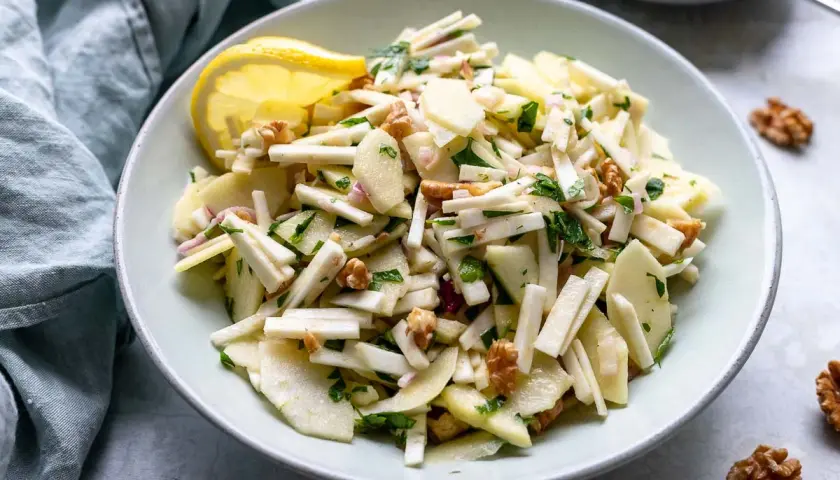 Ein frischer Staudensellerie Salat italienisch mit Äpfeln, Walnüssen und Kräutern, garniert mit einer Zitronenspalte.