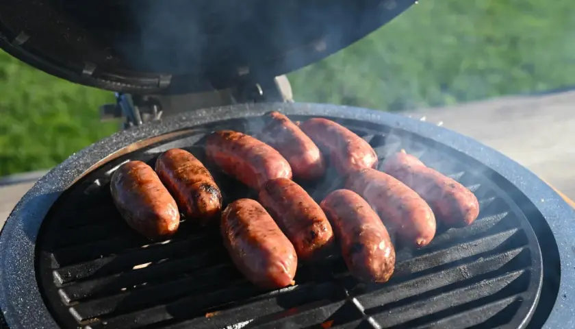 Mehrere Salsiccia brutzeln auf einem Grill. Rauch steigt auf und die Würste bekommen schöne Grillstreifen.