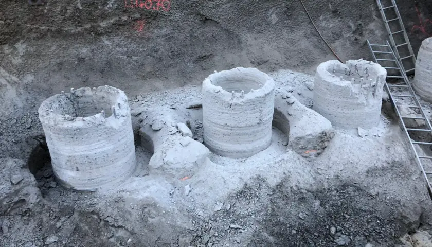 Bohrpfähle ragen aus dem Erdreich, die Reste einer tangierenden bohrpfahlwand. Eine Leiter lehnt an der Wand.