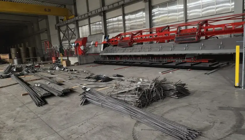 Stal zbrojeniowa w magazynie, gotowa do użycia w budowie. W tle maszyna do produkcji elementów betonowych.