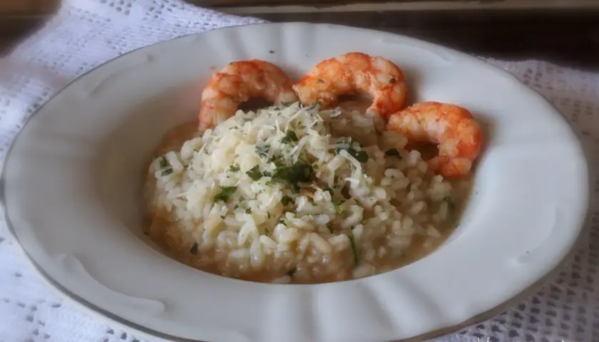 Delicioso risotto de langostinos cremoso, coronado con queso rallado y perejil fresco. Un plato principal que invita a disfrutar.