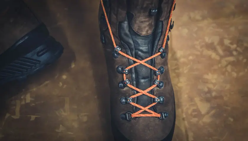 Close-up of a brown hiking boot with bright orange laces tied in a parallel lacing pattern, ready for adventure.