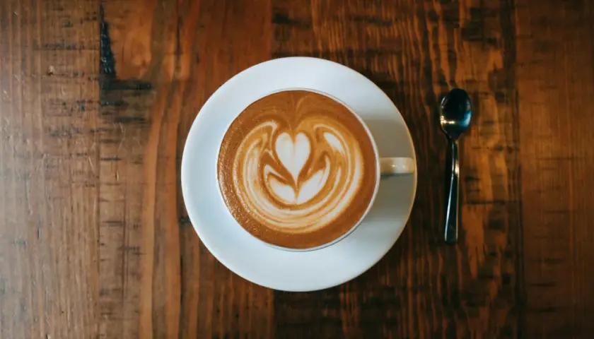 Ein Cappuccino mit Herz-Latte-Art auf einem Holztisch. Woher kommt Cappuccino? Aus Italien, natürlich!