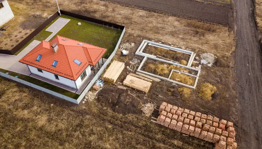 Budowa domu na działce 3 klasy ziemi. Fundamenty, drewno i cegły czekają na realizację warunków zabudowy.