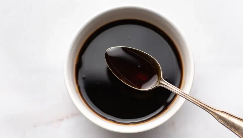 A spoon rests in a bowl of dark liquid, hinting at how to make sweet soy sauce.