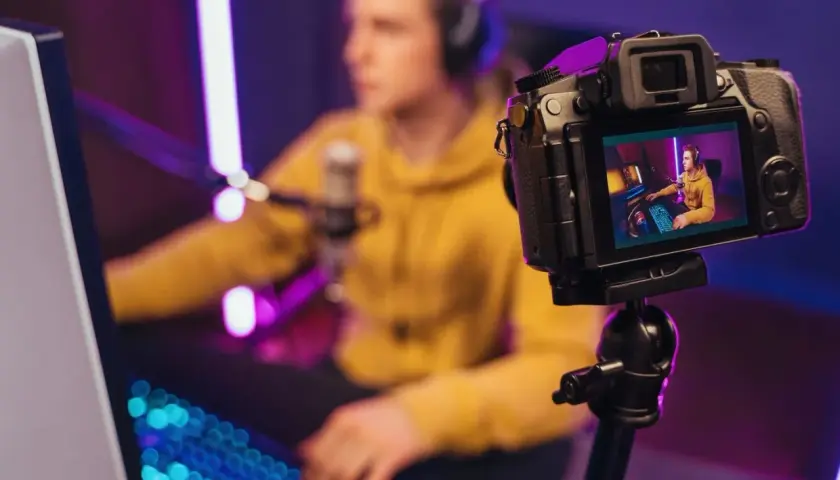 Kamerka do streamowania rejestruje młodego gracza w żółtej bluzie, otoczonego neonowym światłem.