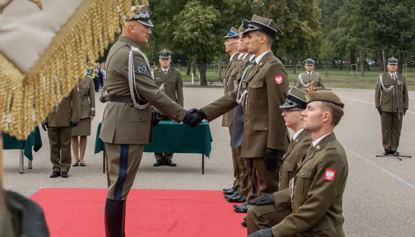 Podporucznik skrót. Uroczystość wręczenia odznaczeń wojskowych. Dwóch oficerów w mundurach ściska sobie dłonie.