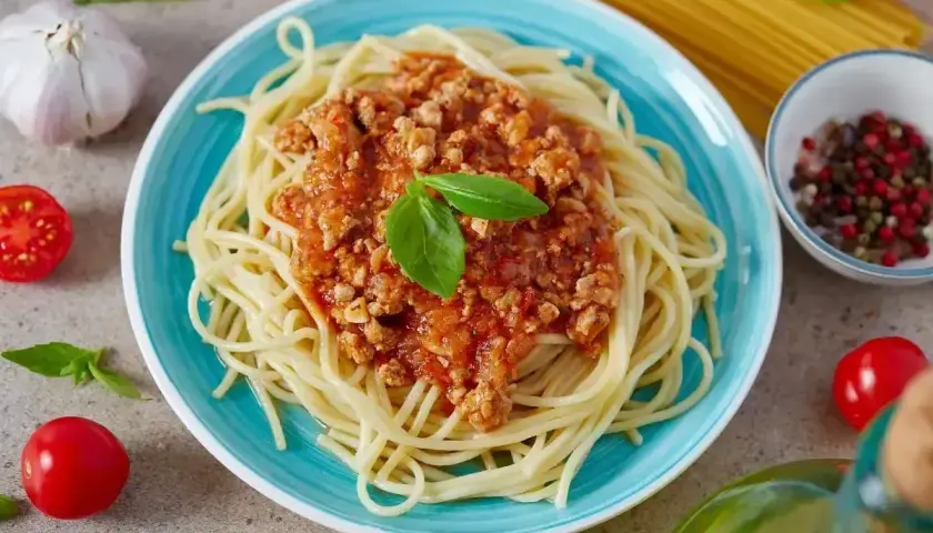 Spaghetti bolognese na talerzu, ozdobione bazylią. Idealne na prosty przepis obiadowy.