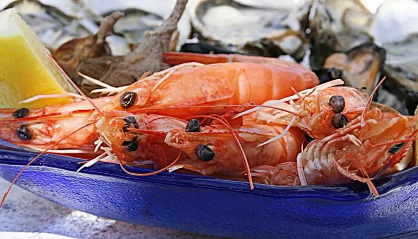 Gambas barbecue sur un plat bleu, avec des huîtres et un quartier de citron en arrière-plan. Un délice de fruits de mer prêt à être dégusté.
