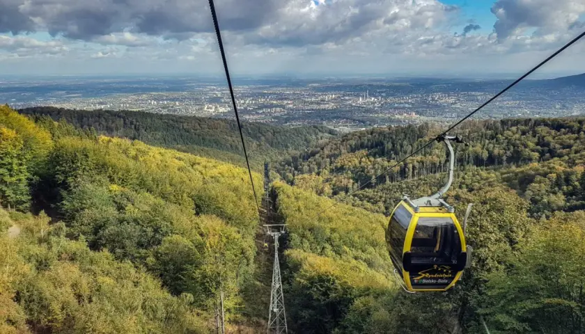 Żółta kolejka linowa z Szyndzielni na Klimczok mija jesienne lasy, a w oddali widać panoramę miasta.