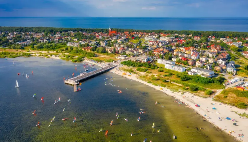 Jastarnia atrakcje dla dzieci: widok na molo, plażę i zatokę pełną żaglowców i desek windsurfingowych.