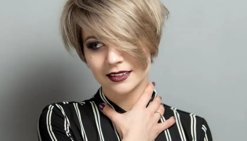 Kobieta z krótkimi blond włosami w stylu pixie, z grzywką na bok, w bluzce w paski.
