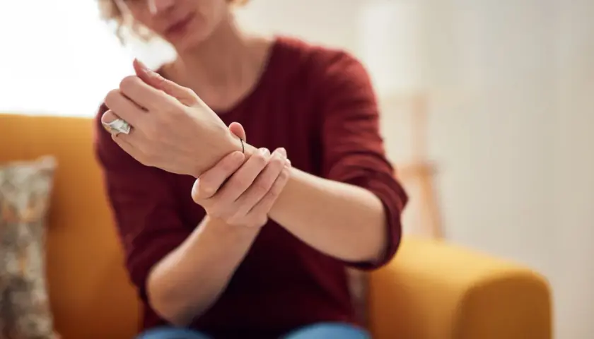 Kobieta z RZS masuje bolące nadgarstki. Praca fizyczna może nasilać objawy.