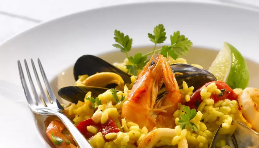 Pyszne risotto z owocami morza: krewetki, małże, kalmary i ryż, udekorowane natką pietruszki i ćwiartką limonki.