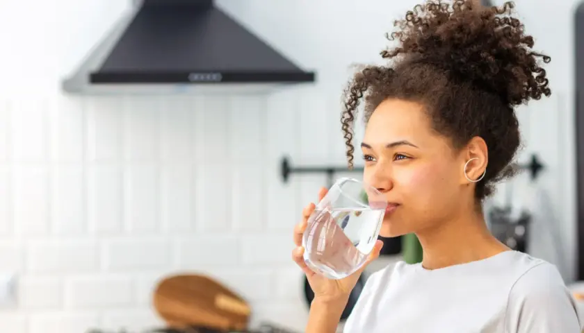 Donna sorseggia un bicchiere d'acqua, un rimedio naturale per la stitichezza.