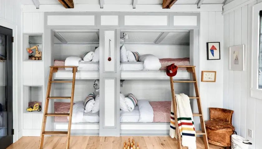 A cozy built in bunk room with four beds, wooden ladders, and playful decor like toy excavators and bowling pins.