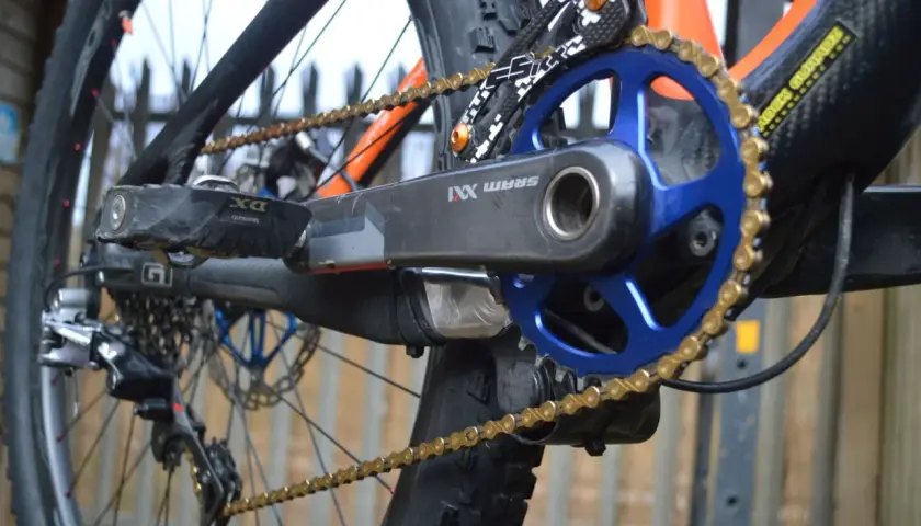 Close-up of a mountain bike's drivetrain, featuring a SRAM XX1 chain, blue chainring, and black crank arm.