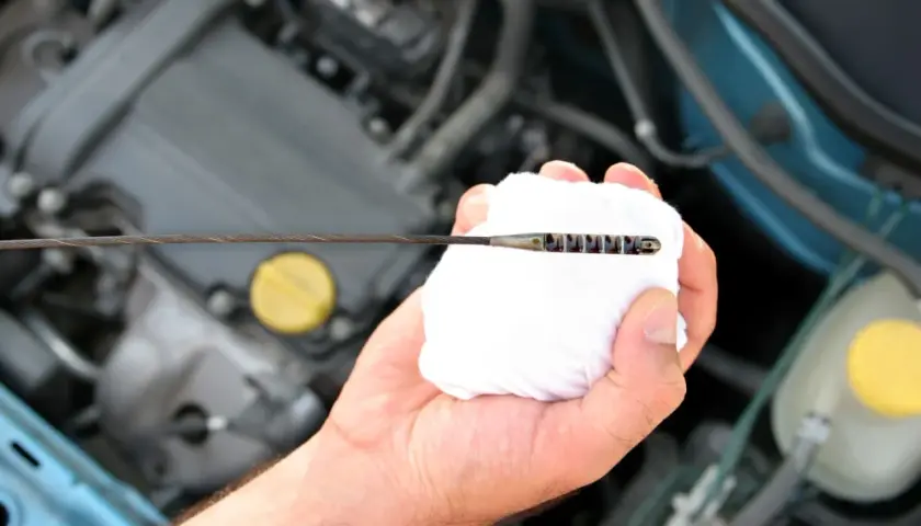 Mano limpiando la varilla del nivel de aceite en el motor. El aceite está entre las marcas de mínimo y máximo.