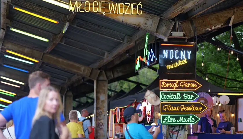 Nocny market Warszawa wita neonami: "Miło Cię Widzieć", "Drugi Peron", "Cocktail Bar", "Piano Sessions", "Live Music".