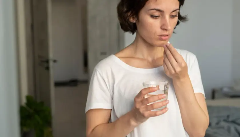 Mujer toma pastilla con agua, pensando en cuando tomar probióticos con antibióticos para cuidar su salud intestinal.