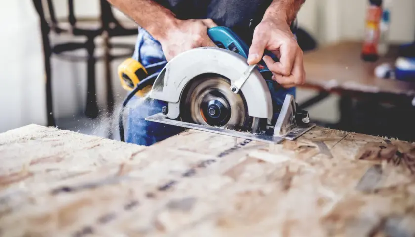 Ein Handwerker sägt mit einer **Baukreissäge** Holz. Sägespäne fliegen durch die Luft.