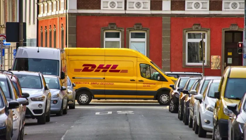 Żółta furgonetka DHL zaparkowana na ulicy, obok inne samochody. Może być potrzebny protokół szkody.