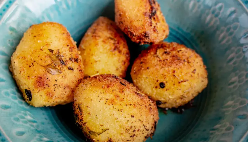 Fem gyllene, rostad potatis i ugn, kryddade med örter och peppar, serveras i en vacker turkos skål.