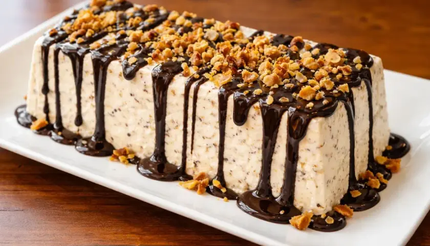 Parfait dolce a forma di panettone, ricoperto di cioccolato fuso e granella di nocciole croccanti.