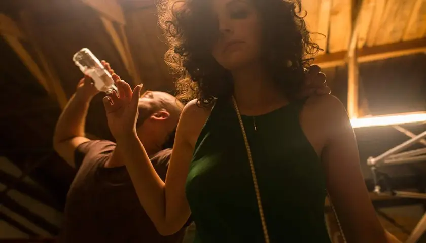 Kobieta w zielonej sukience i mężczyzna pijący z butelki. Scena jak z filmu, pełna zabawy i emocji.