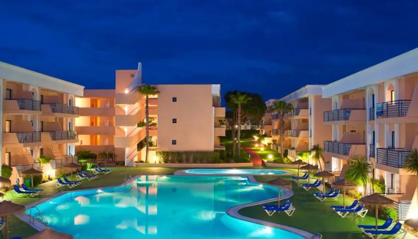 Resort con piscina iluminada y edificios de apartamentos bajo el cielo nocturno. Un lugar perfecto para disfrutar del sol Sancti Petri.