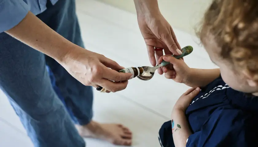 Mama podaje dziecku łyżeczkę z kroplami psychobiotyku. Dziecko z zaciekawieniem patrzy na podawany specyfik.