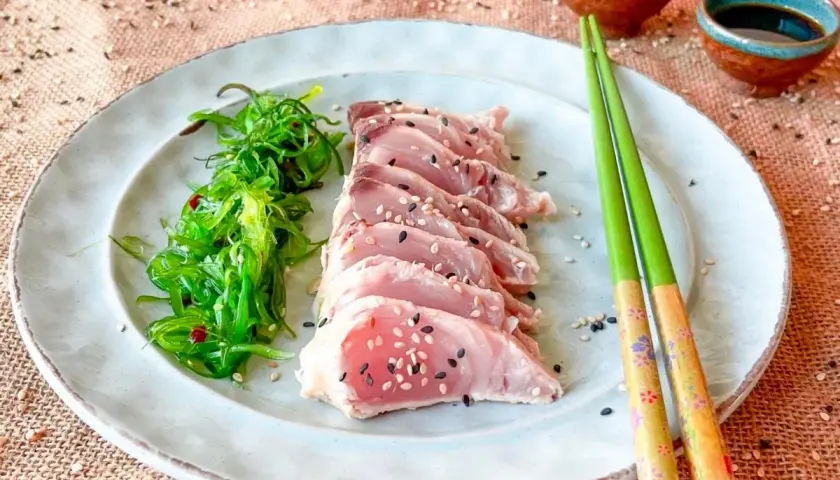 Tataki de bonito, finas lonchas de pescado rosado con semillas de sésamo, acompañadas de ensalada de algas.