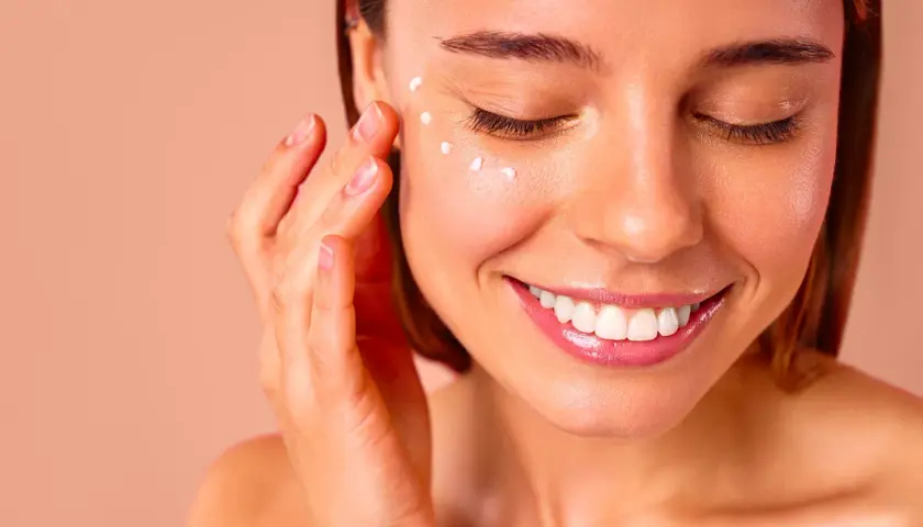 Une femme applique de la crème autour de ses yeux, un geste doux pour un massage des yeux relaxant.