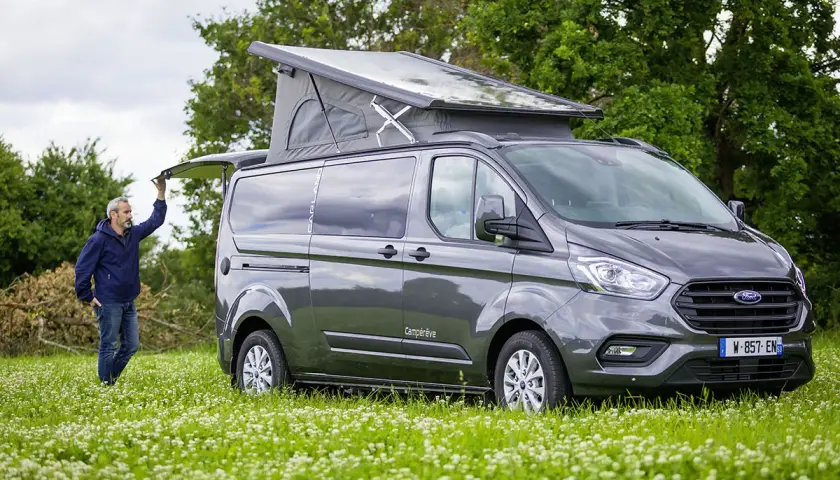 Un homme ouvre le hayon d'un van aménagé avec toilette, prêt pour l'aventure en pleine nature.